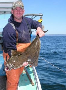photo of a man holding a halibut aboard a boat