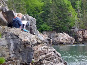 a young camper sitting on a rock by the sea