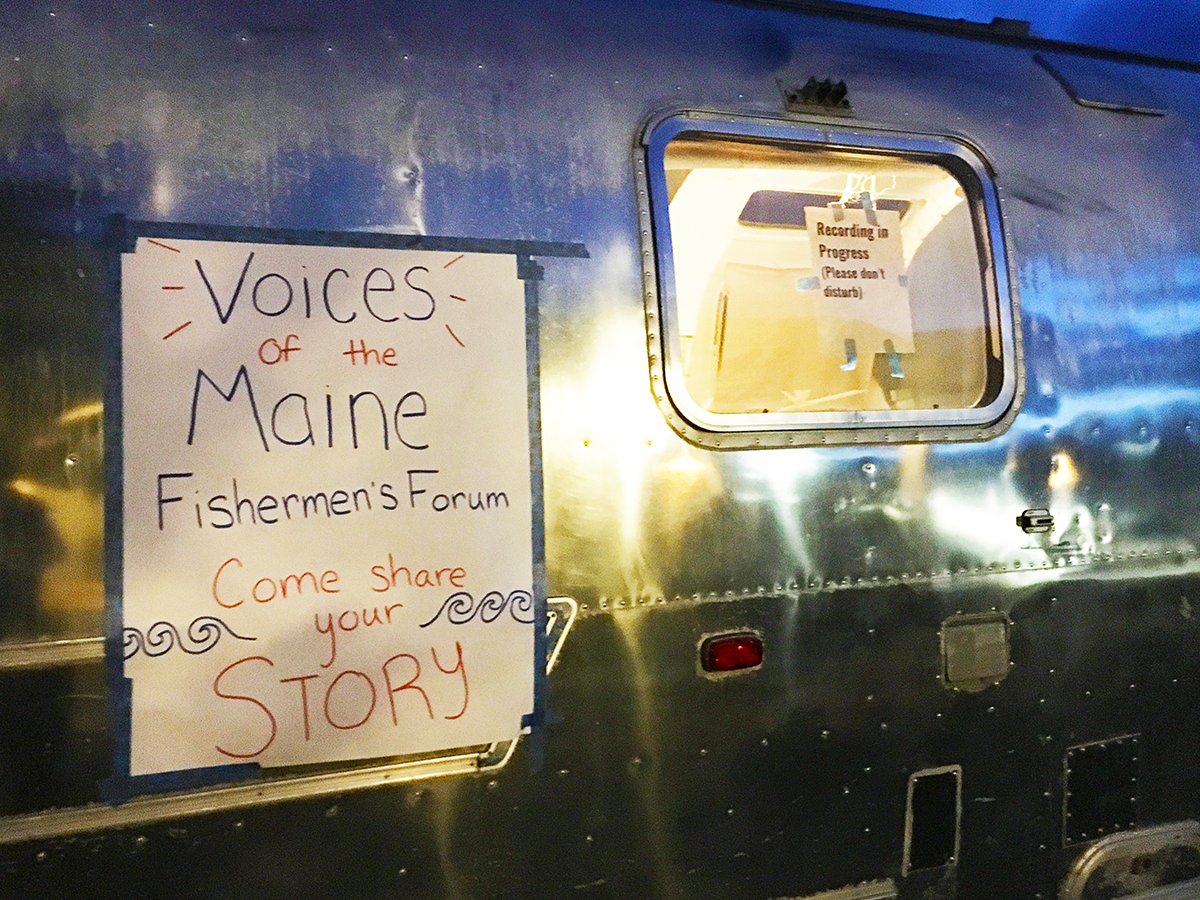 A handwritten sign on the window of an Airstream trailer reading 'Voices of the Maine Fishermen's Forum - Come share your story'