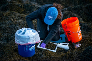 a person kneeling on rockweed surrounded by buckets