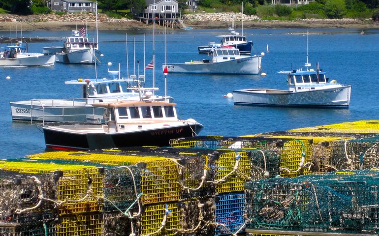 lobster boat in water behind stacked traps on shore