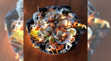 Bowl with scallops, noodles, salad greens, carrots, hard-boiled eggs, and other food items. The bowl is set on a wooden surface. 
