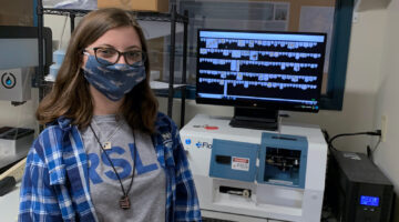 Masked photo of Tessa in front of a computerized display
