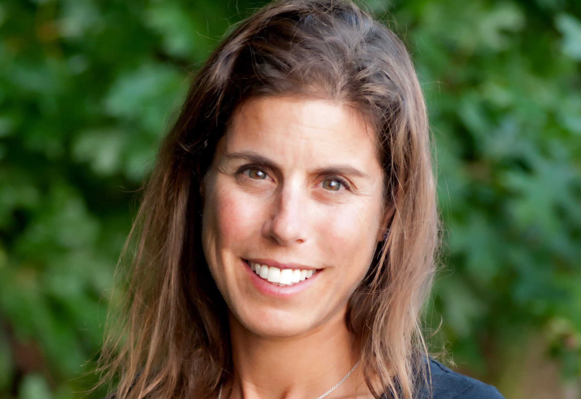 Woman looking at camera and smiling with green foliage in the background