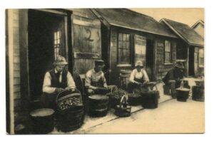 Four men sitting in front of buckets full of shellfish with empty buckets next to each of them.