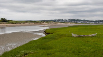 Wooden dory rests on coastal grass next to a tidal river