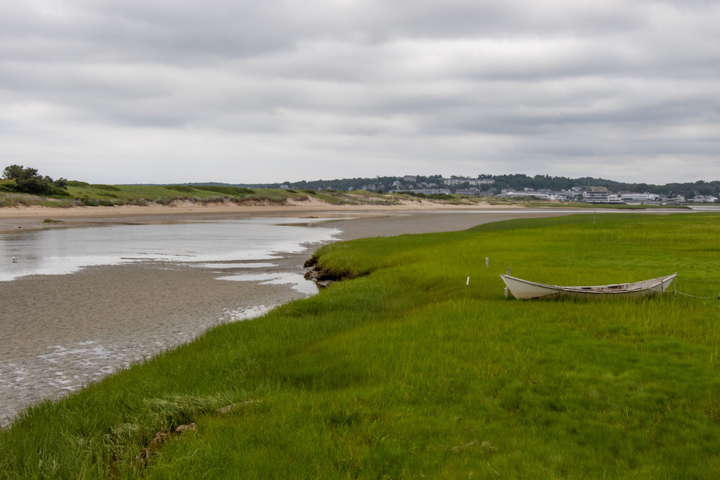 Wooden dory rests on coastal grass next to a tidal river