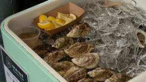 Oysters on a half-shell, on ice and a brown container with lemon wedges.