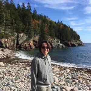 Gayle Zydlewski on a rocky shore in front of evergreens under a blue sky