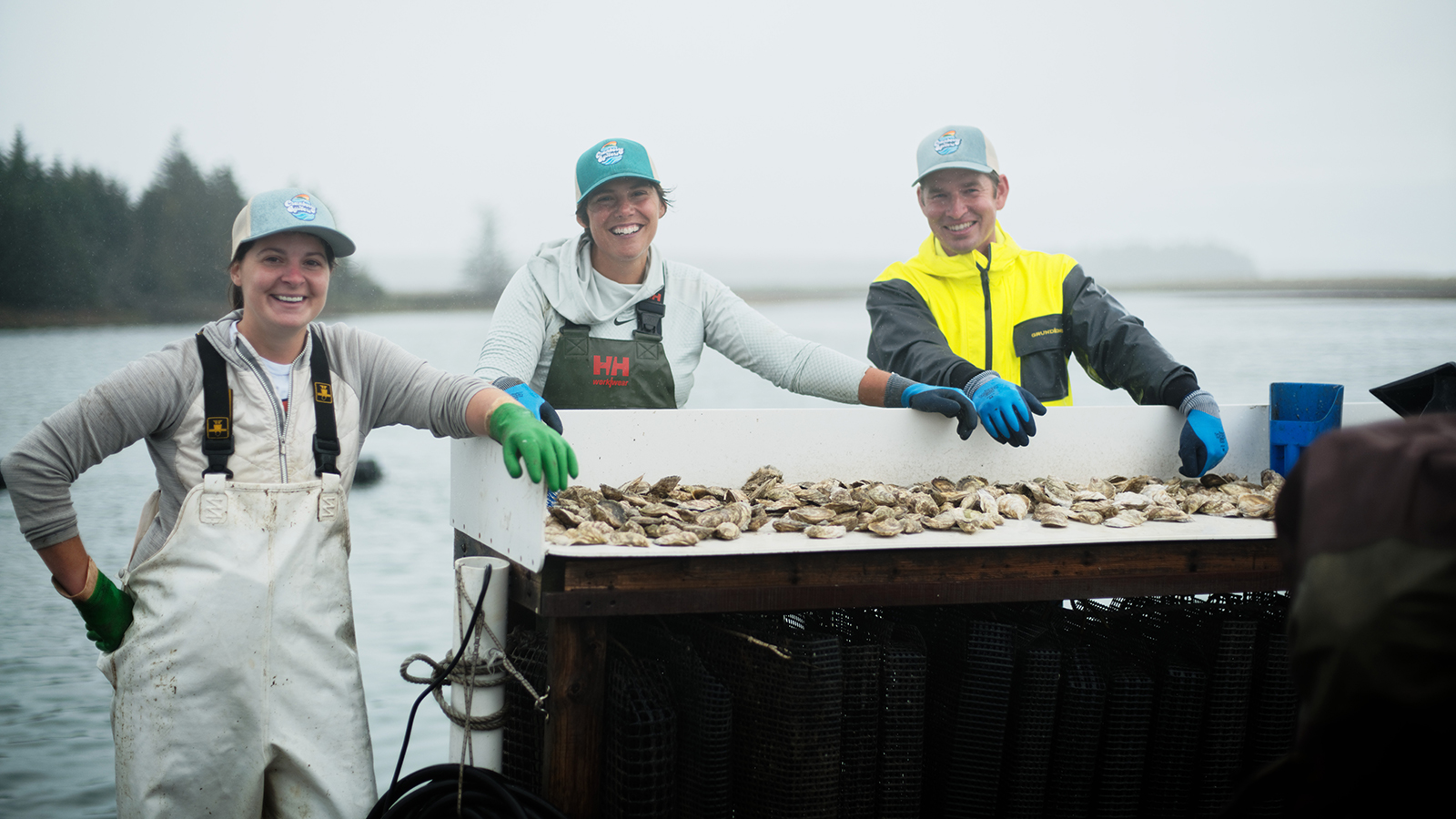 three marine farmers standing before a table of shellfish