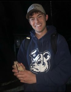 a person in a cap and sweatshirt at night holding a bird