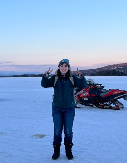 Andi Rudai in winter giving peace signs in front of a snowmobile