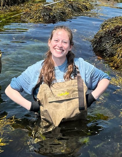 Nicole Snow in chest waders waist deep in water surrounded by seaweed