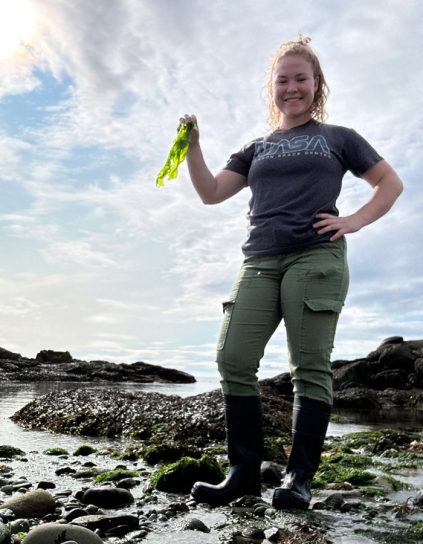 Sophia Tearman holding kelp on the rocky shore.