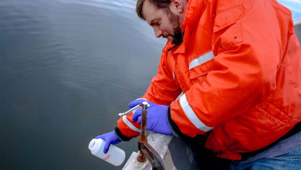 Justin Stevens collects water in an orange coat off the side of a vessel. 