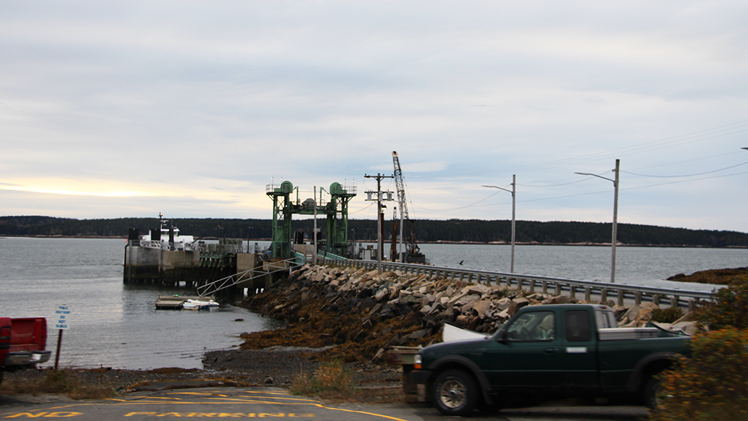 A photograph of Swan’s Island’s green ferry terminal, a large pier of piled stones with the ferry and a construction barge at the end. Fisheries products from the island are brought to markets on the mainland by the Maine state ferry service.