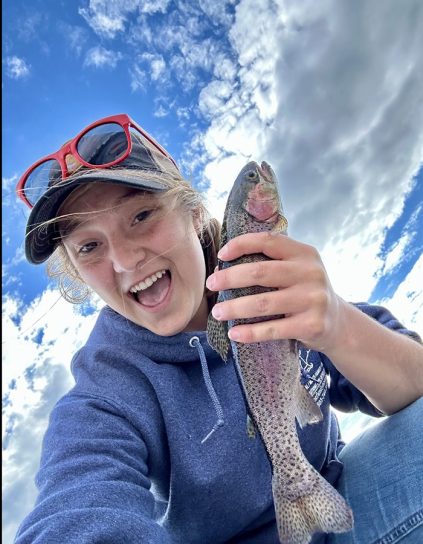 Emily Coulombe selfie holding a fish with blue sky and clouds behind her