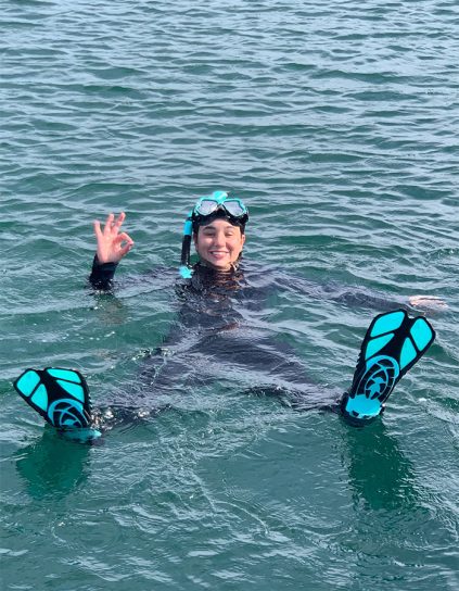 Delphine Demaisy in dive gear in the water giving the OK symbol with her hand