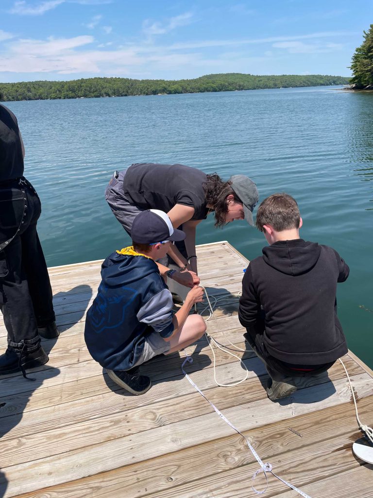 A teacher and two students kneeling on a dock.