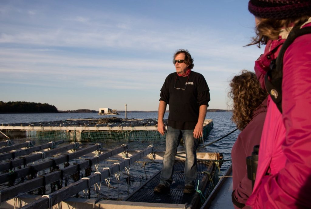 A mussel farmer stands on the water in his raft as he answers a tour group's questions.