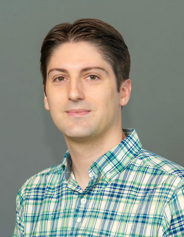 headshot of Georgios Boumis grey background wearing a green and blue checked shirt