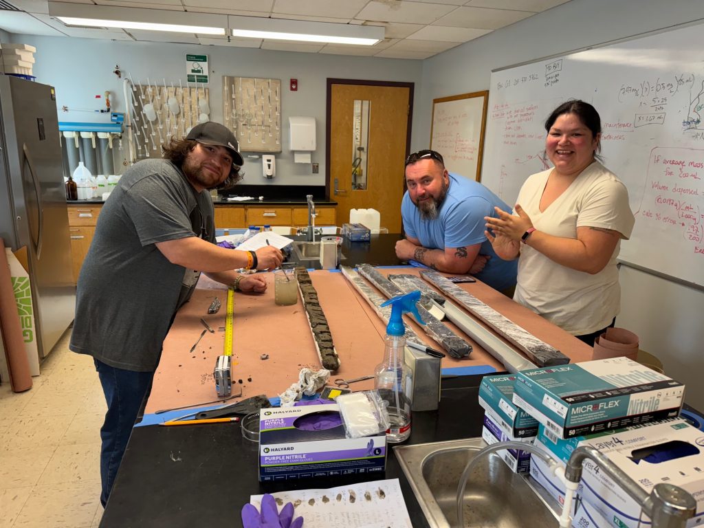 Three people smile for the camera while working over a table in a lab.