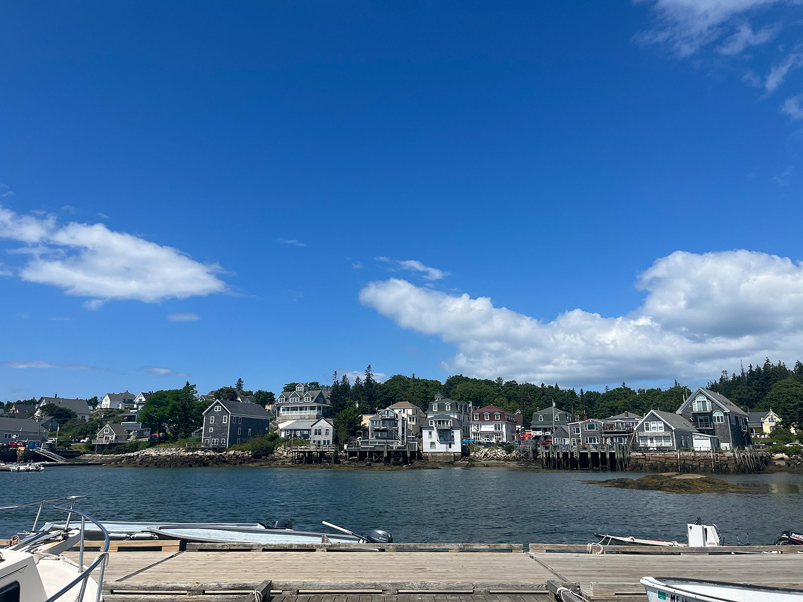 blue sky with a few clouds, buildings on shore across the water as viewed from a weathered dock.